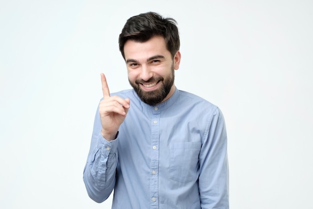 Uomo in camicia blu che punta verso l'alto con il dito isolato su sfondo grigio