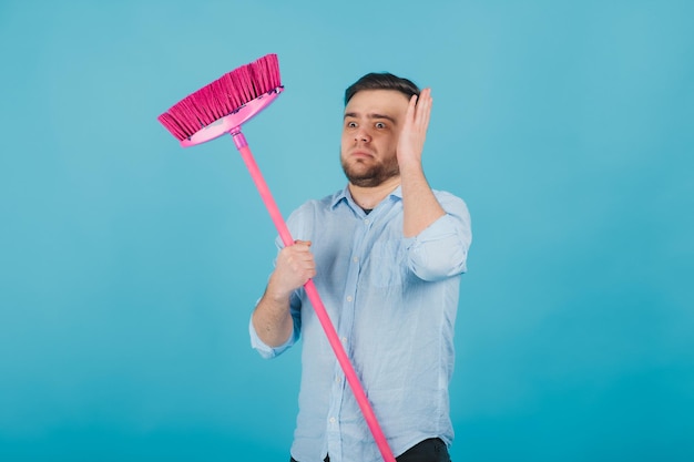 uomo in camicia blu si erge su sfondo blu con scopa rosa