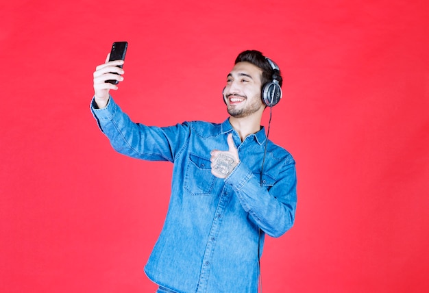 Uomo in camicia di jeans che indossa le cuffie, si fa un selfie o fa una videochiamata.