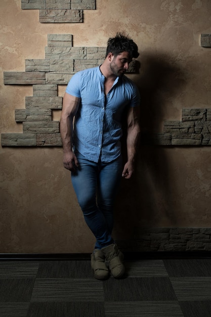 Uomo in camicia di jeans in piedi su uno sfondo di mattoni