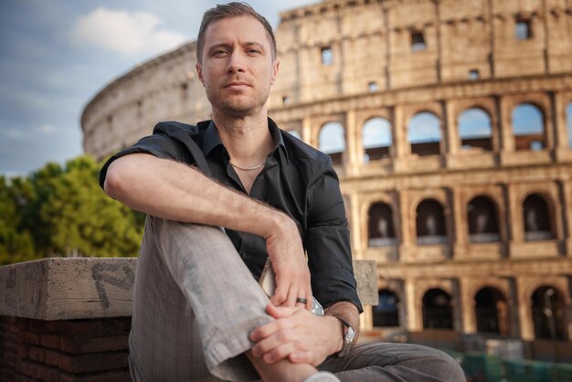 Uomo in camicia nera seduto di fronte al Colosseo all'alba in Italia