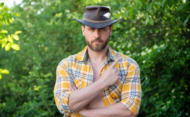 Uomo in cappello da cowboy uomo sexy in camicia a scacchi uomo occidentale che indossa il cappello punta il dito