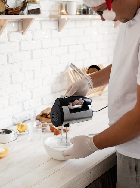 Uomo in cappello della Santa che monta i bianchi d'uovo con il miscelatore elettrico in cucina