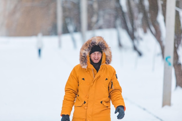 Uomo in cappotto invernale giallo con cappuccio che cammina nel parco innevato