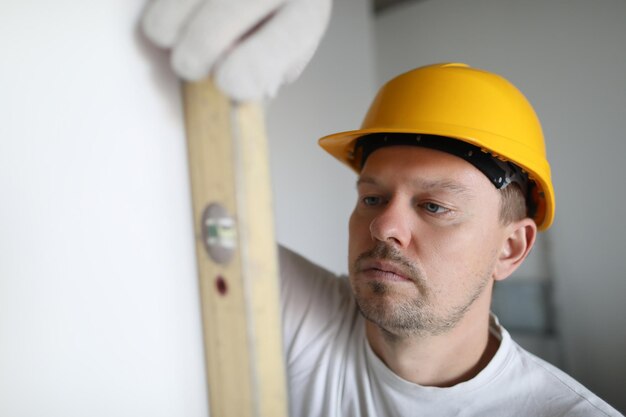 Uomo in casco che misura la parete usando il livello dell'edificio in appartamento