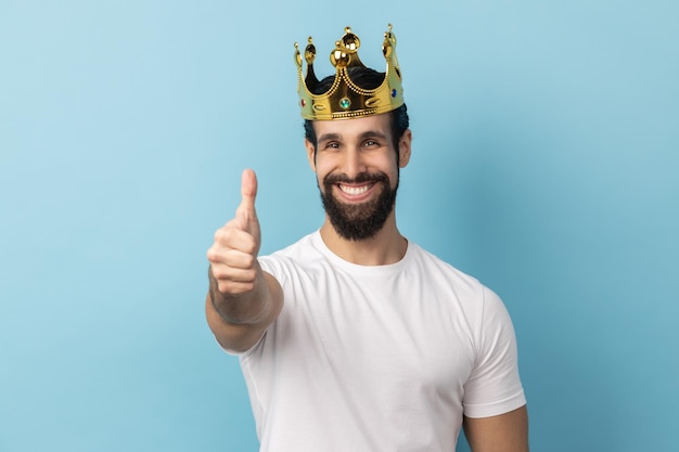 Uomo in corona d'oro in piedi che guarda l'obbiettivo con un sorriso a trentadue denti che mostra il pollice in su