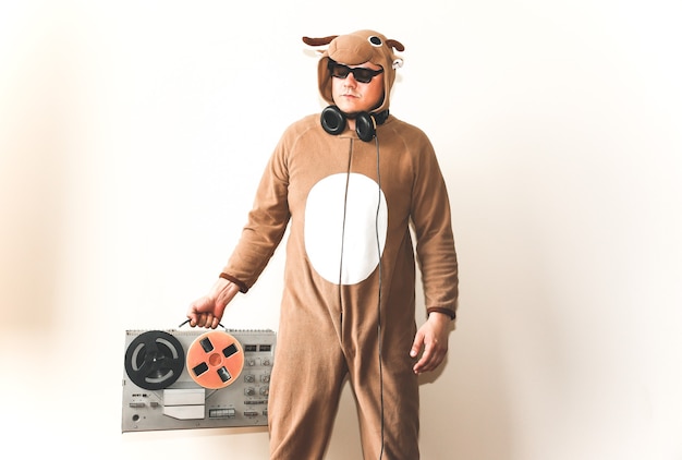 Uomo in costume cosplay di una mucca con registratore a bobina. Ragazzo negli indumenti da notte del pigiama animale. Foto divertente con idee per feste. Musica retrò da discoteca.