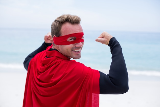 Uomo in costume da supereroe che flette i muscoli in riva al mare