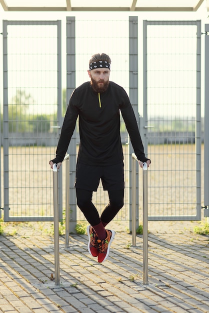 Uomo in forma che fa i tricipiti sulle barre parallele al parco che si esercita all'aperto