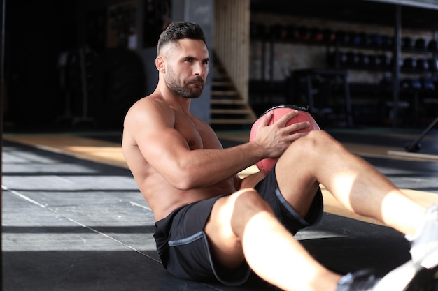 Uomo in forma e muscoloso che si esercita con la palla medica in palestra.