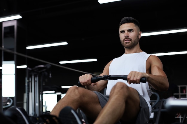 Uomo in forma e muscoloso che utilizza vogatore in palestra.