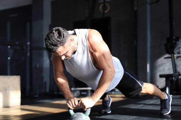 Uomo in forma e muscoloso concentrato sul sollevamento di un manubrio durante una lezione di ginnastica in palestra.