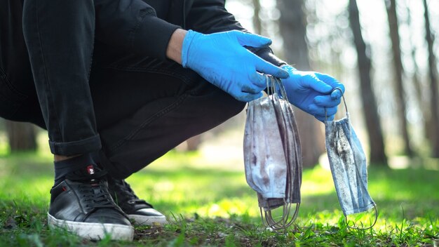 Uomo in guanti medicali raccogliendo maschere mediche sporche da terra in un parco