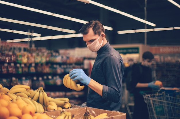 Uomo in guanti protettivi che scelgono le banane in un supermercato. igiene e sanità