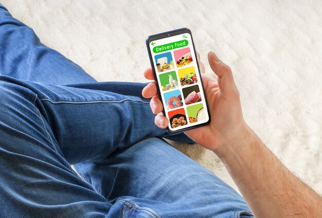 Uomo in jeans sdraiato sul divano e in possesso di telefono con cibo di consegna app sullo schermo. Concetto di ordine alimentare.