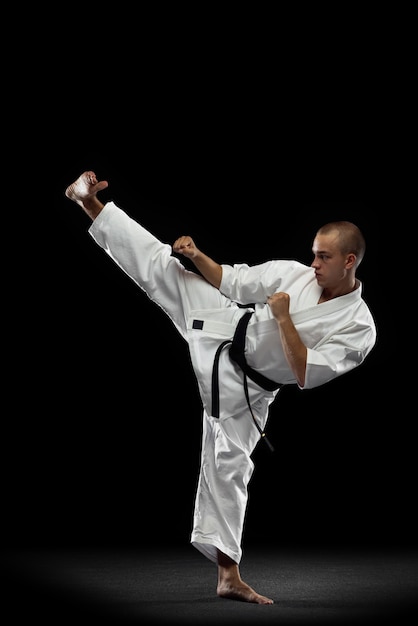 Uomo in kimono bianco e cintura nera di addestramento di karate su sfondo grigio.