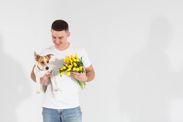 Uomo in maglietta bianca che sta con i fiori e il cane.