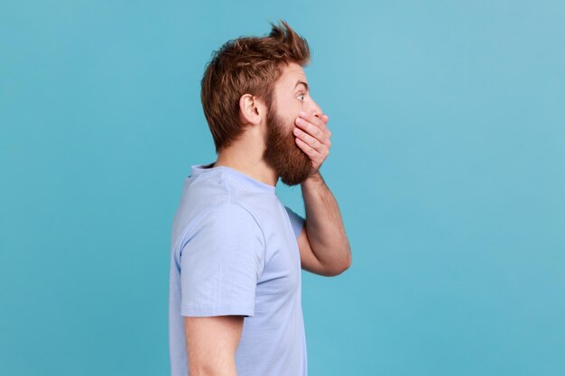 Uomo in maglietta blu che chiude la bocca mantenendo le informazioni segrete guardando lo spazio laterale