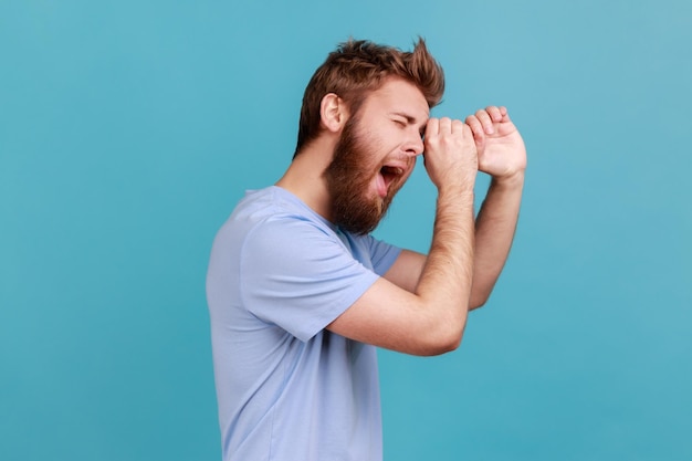 Uomo in maglietta blu che fa un gesto monoculare con le mani e guarda stupito lo spazio laterale