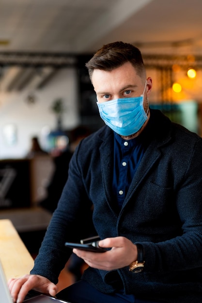 Uomo in maschera che lavora al telefono durante la quarantena. Uomo alla moda che si trova sui social media in quarantena.