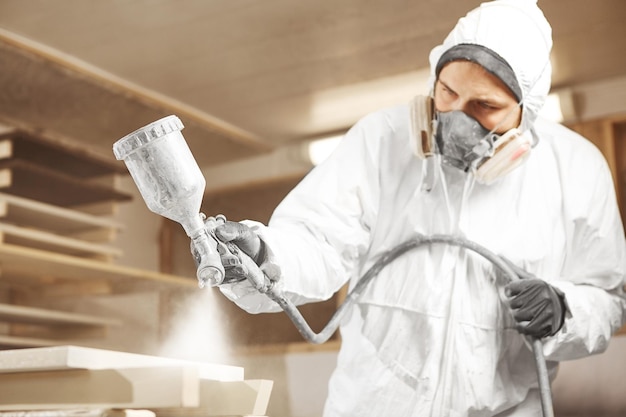 Uomo in maschera respiratoria che dipinge assi di legno in officina