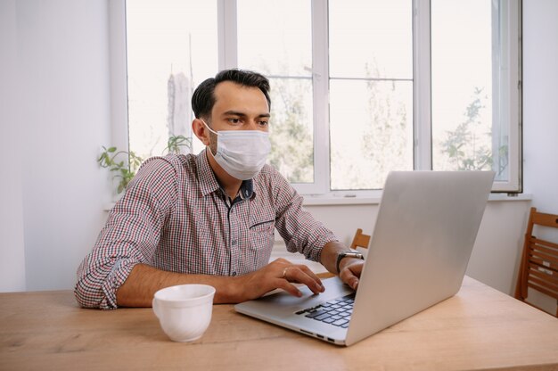 Uomo in mascherina medica utilizzando laptop a casa