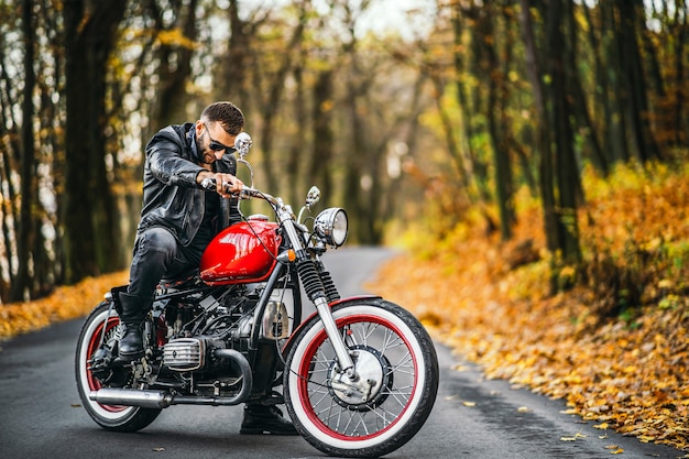 Uomo in occhiali da sole e giacca di pelle che si siede su una moto sulla strada