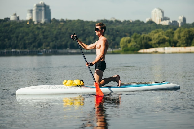 uomo in occhiali da sole e pagaia a bordo sup sul fiume sullo sfondo di un bellissimo paesaggio