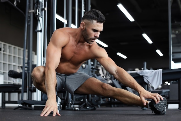 Uomo in palestra facendo esercizi di stretching sul pavimento.