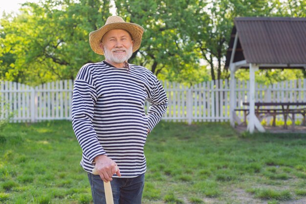 Uomo in pensione sorridente. Trasmissione via IR di un uomo in pensione che indossa un cappello di paglia che sorride prima di scavare il suo orto