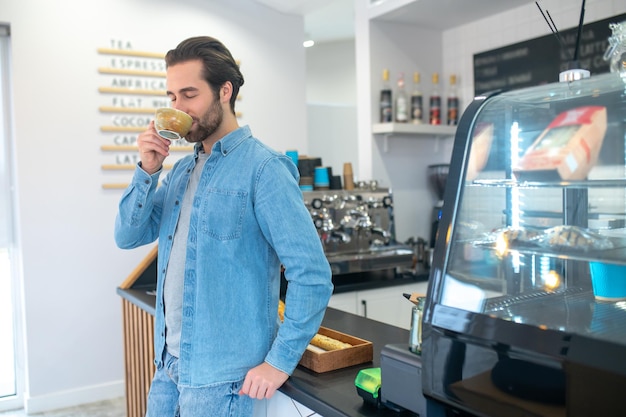 Uomo in piedi che beve caffè con gli occhi chiusi