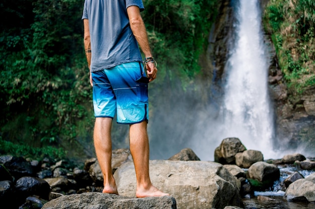 Uomo in piedi da un fiume davanti a una cascata. Turrialba, Costa Rica