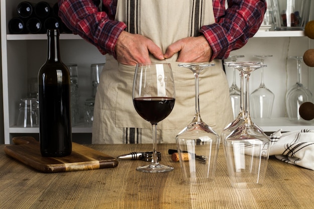 Uomo in piedi davanti a un tavolo di legno con un bicchiere di vino rosso