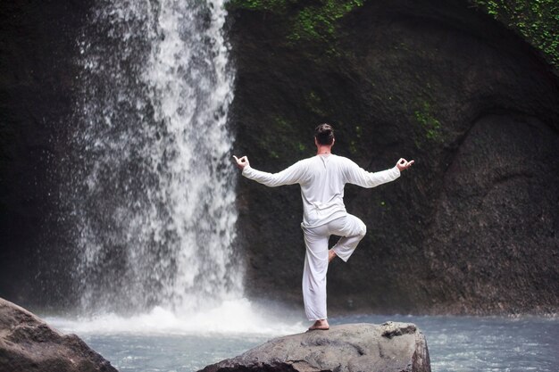 Uomo in piedi in meditazione yoga su roccia a cascata in Bali . tropicale