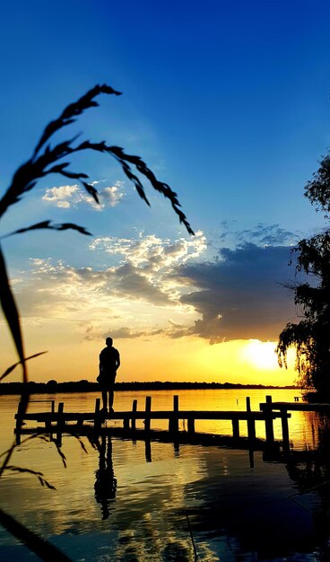 Uomo in piedi sul molo contro il tramonto sagoma scura di erba