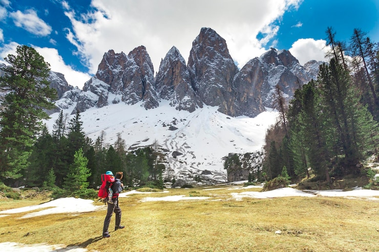 Foto uomo in piedi sull'erba con le montagne coperte di neve contro il cielo