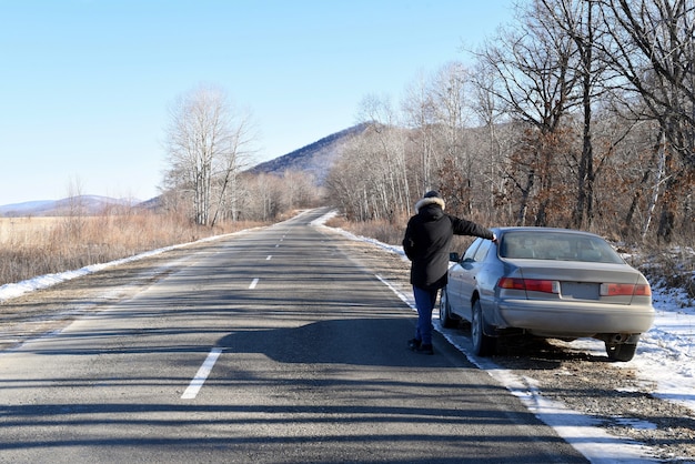 Uomo in piedi sulla strada accanto alla sua auto guardando avanti