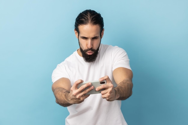 Uomo in piedi utilizzando lo smartphone e giocando a giochi per cellulare con la faccia eccitata concentrata