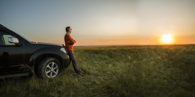 uomo in piedi vicino a un'auto fuoristrada in vacanza e guardando il tramonto sul banner della natura con spazio per la copia