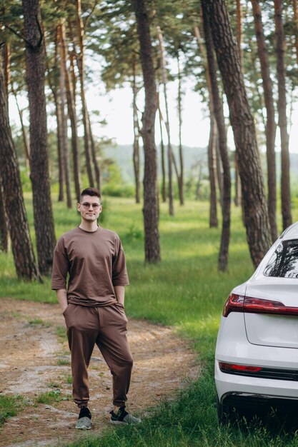 Uomo in piedi vicino all'auto nella foresta nella stagione autunnale dello spazio della copia della strada del sentiero