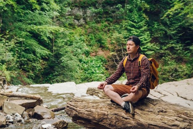 uomo in posizione meditativa seduto su un tronco d'albero sullo sfondo della foresta e del fiume