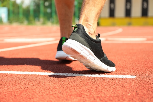 Uomo in scarpe da tennis sulla pista corrente atletica rossa, fine su