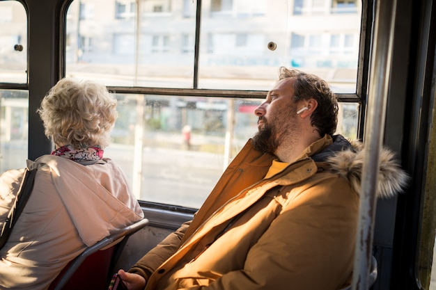 Uomo in trasporto pubblico che si siede con lo smartphone che ascolta la musica