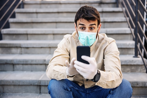 Uomo in tuta protettiva con maschera che digita sul telefono cellulare dello smartphone, infezione da virus, contaminazione di germi o batteri. Prevenzione delle infezioni e controllo dell'epidemia.