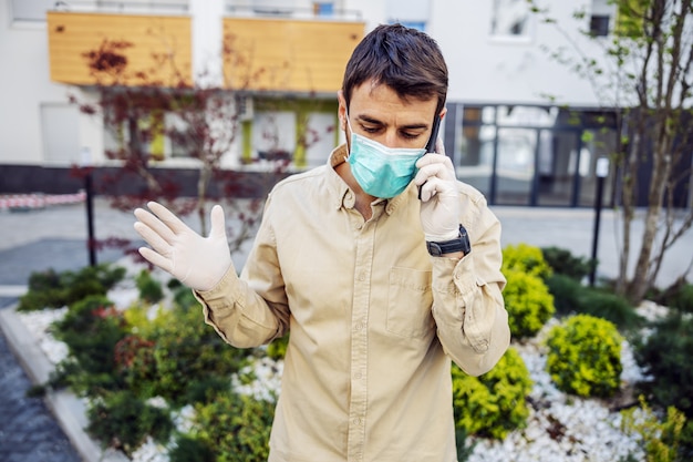 Uomo in tuta protettiva con maschera parlando al cellulare dello smartphone, infezione da virus, contaminazione di germi o batteri. Prevenzione delle infezioni e controllo dell'epidemia.