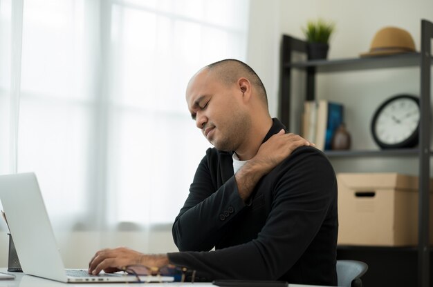 Uomo in tuta seduto a casa a lavorare con il computer portatile ha dolore al collo alla spalla