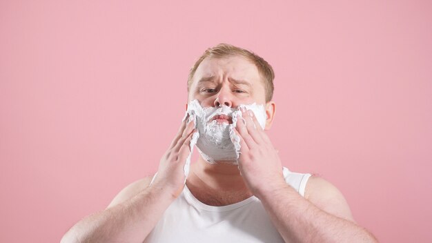 Uomo in un corpo con schiuma da barba sulle guance, un uomo in procinto di radersi, foto isolata su uno sfondo rosa