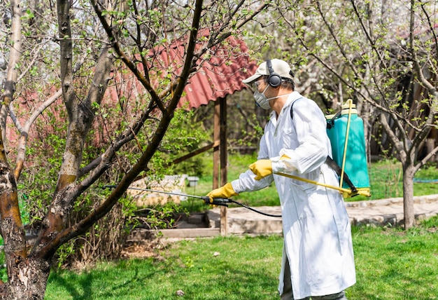 Uomo in un giardino con zaino spruzzatore a pressione che protegge gli alberi da parassiti e malattie fungine