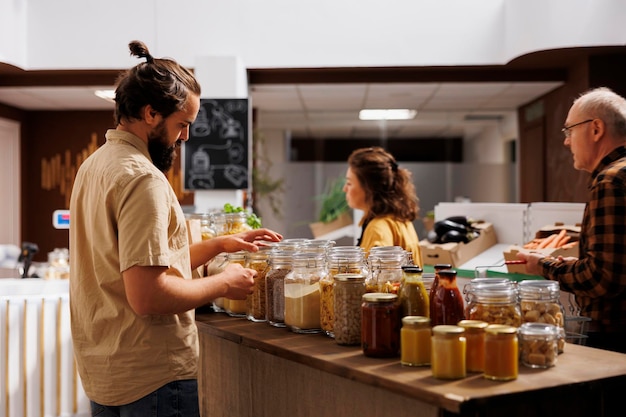 Uomo in un negozio a rifiuti zero rispettoso dell'ambiente interessato all'acquisto di alimenti ad alto valore nutrizionale. Cliente alla ricerca di prodotti di base da dispensa in imballaggi riutilizzabili in un negozio di alimentari locale