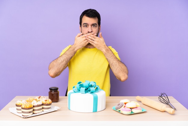 Uomo in un tavolo con una grande torta che copre la bocca con le mani